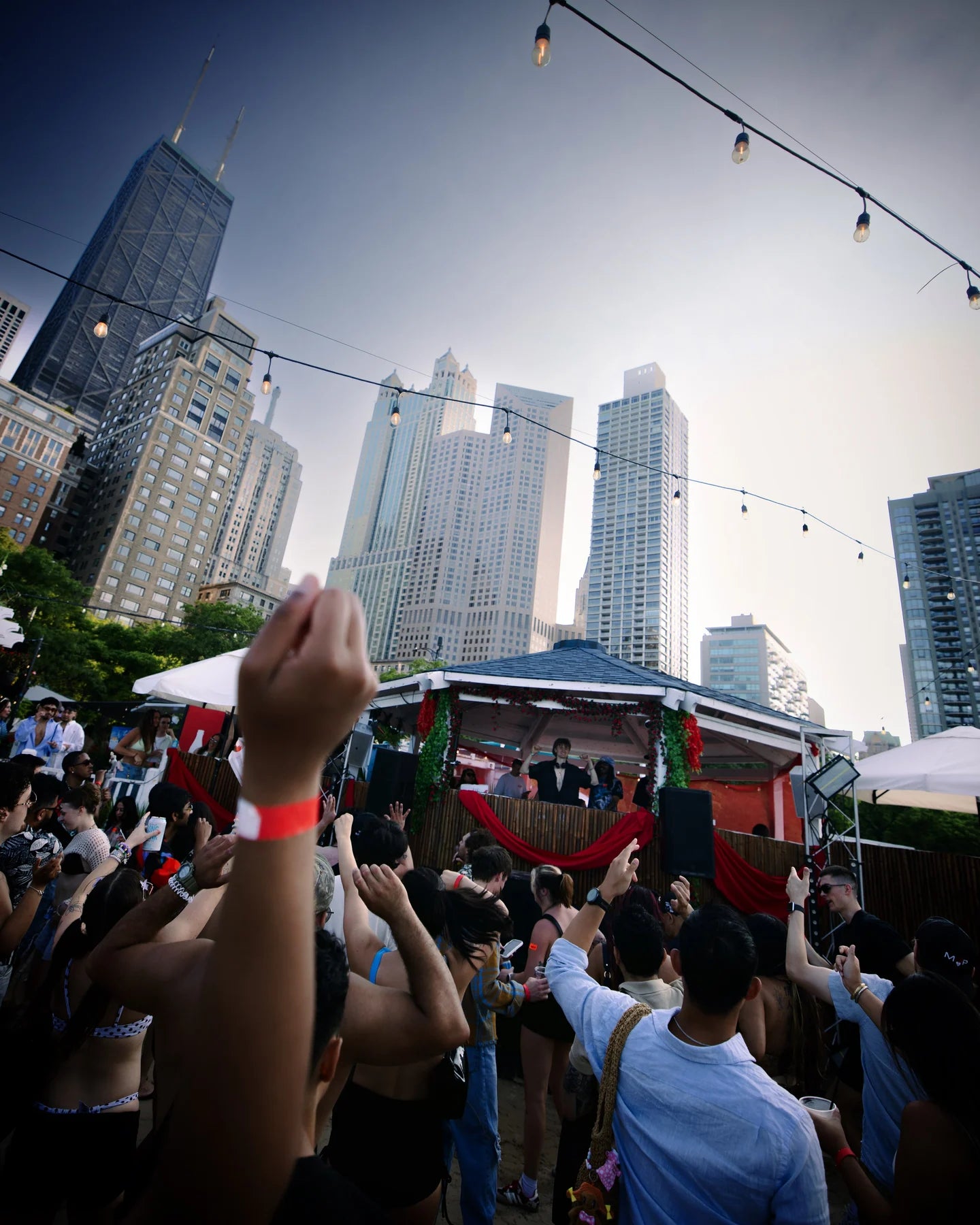 An outdoor crowd raises hands toward a pavilion with Chicago high-rises behind it.